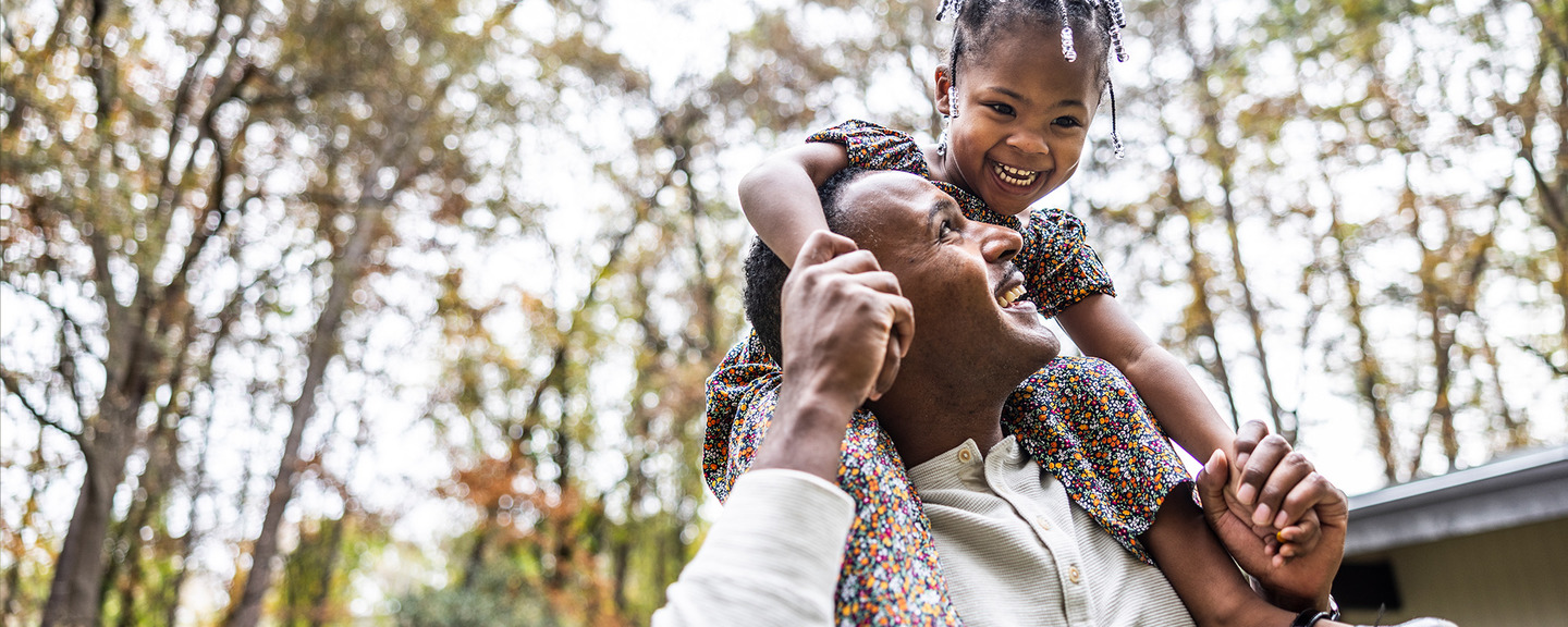 Father giving young daughter a piggyback ride in front of suburban home